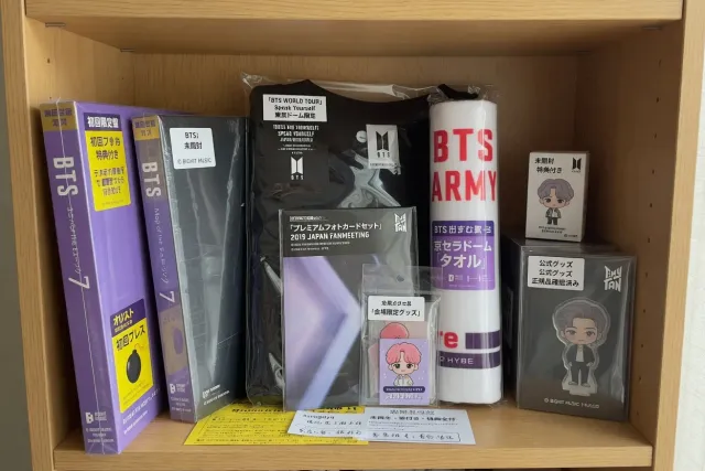 Official BTS merchandise from Japan including sealed albums, concert goods, and character items displayed on a shelf