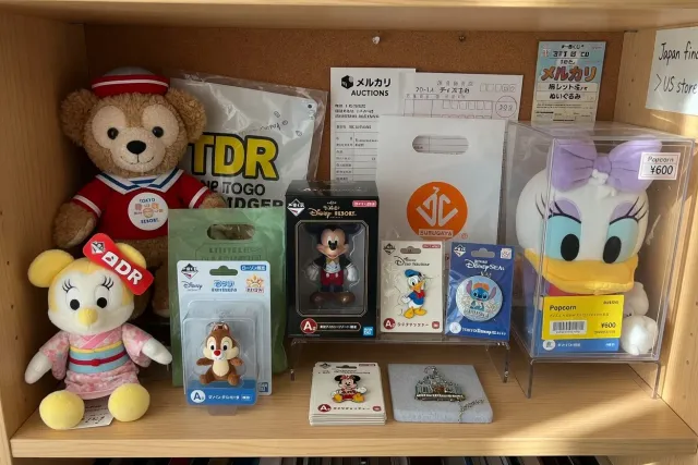 Disney merchandise from Japan including character plush, figures, pins, and Tokyo Disney Resort goods displayed on a collector shelf