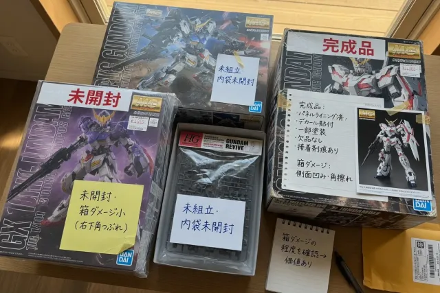 Close view of Gundam model kits from Japan with sealed boxes, box damage notes, and HG and MG grade labels