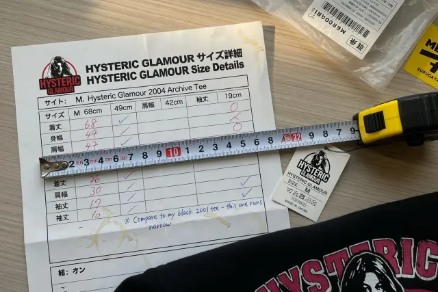 Close-up of a Hysteric Glamour shirt measurement chart beside a tape measure and garment tag