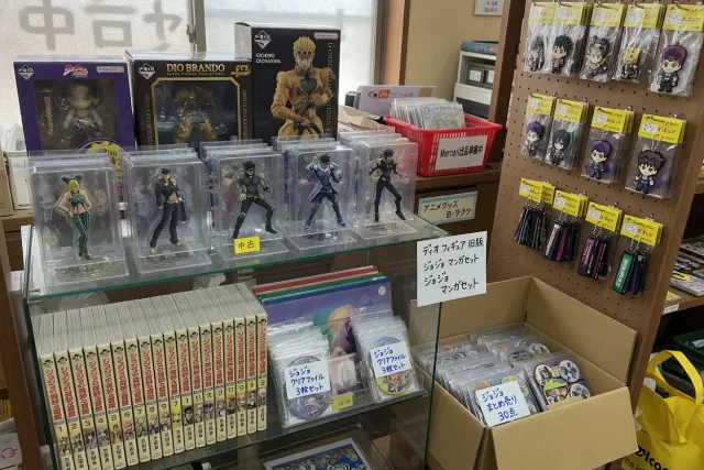 JoJo's Bizarre Adventure merchandise display with figures, acrylic stands, manga, and character keychains in a Japanese resale shop