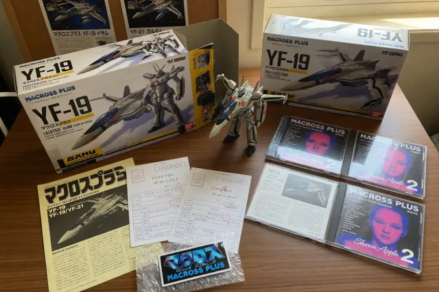 Macross Plus merchandise display with YF-19 figures, soundtrack CDs, and Japanese collector items