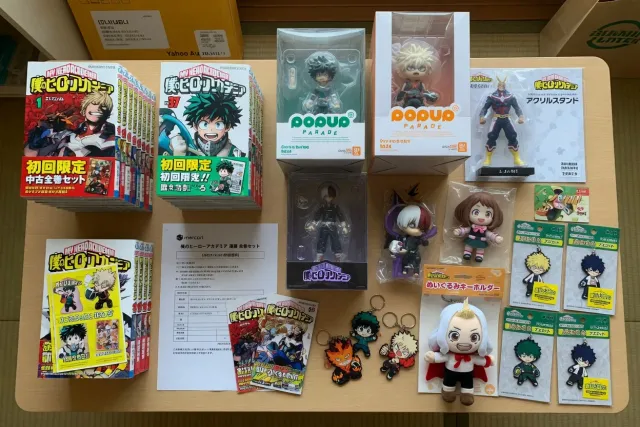 A Japanese My Hero Academia merchandise display with manga volumes, character figures, acrylic stands, plush, and keychains