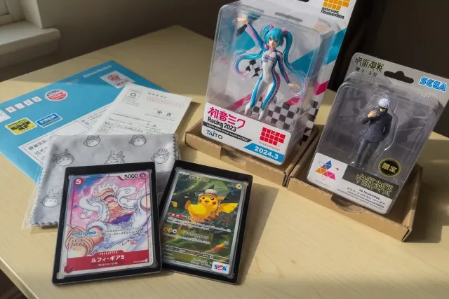 Close-up of rare Japanese Pokémon cards in protective sleeves beside collectible Pokémon prize figures