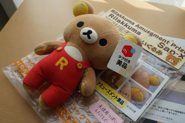 Close-up of a pre-owned Rilakkuma plush toy listing showing tags, fabric condition, and original packaging