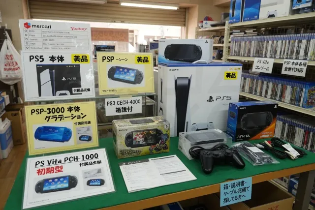 Japanese Sony PlayStation console listings displayed beside boxed games and controllers in a resale shop