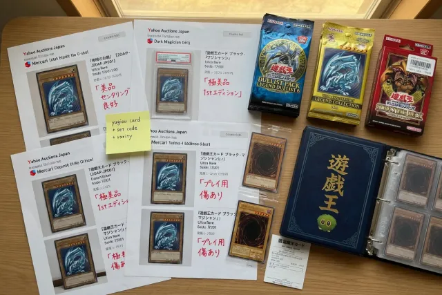 Japanese Yu-Gi-Oh! card listings displayed beside sealed booster packs and trading card binders